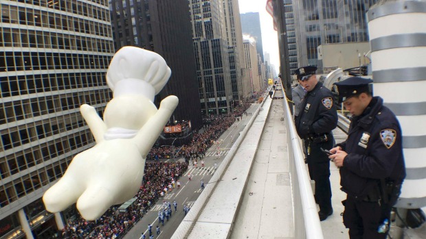 New York Police Department officers stand watch from a building as a float of the Pillsbury Doughboy proceeds high above spectators along 6th Ave