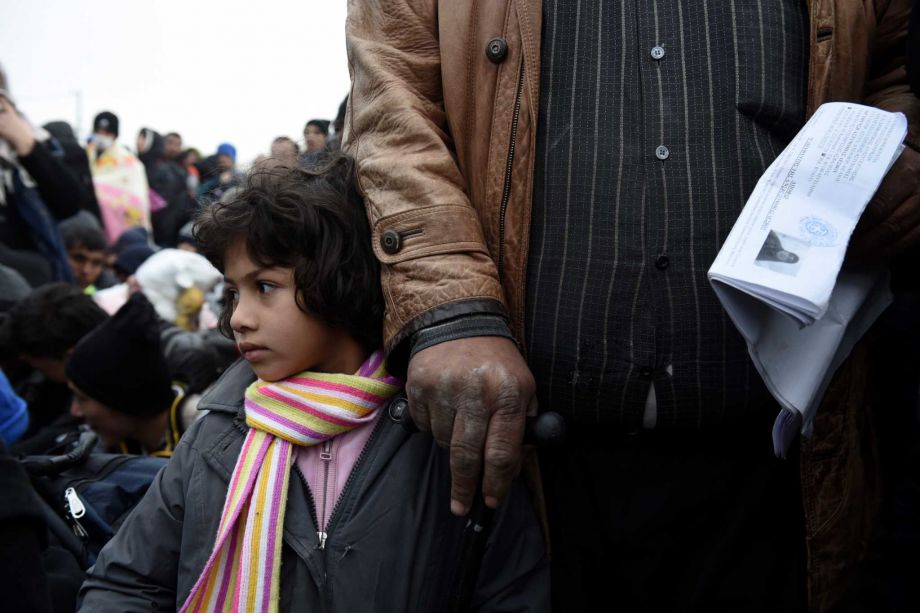 A Syrian girl with her father wait to be allowed by the Greek police to cross the borderline to Macedonia near the village of Idomeni Saturday Nov. 21 2015. Tempers have flared at Greece's main border crossing with Macedonia where riot police pushed