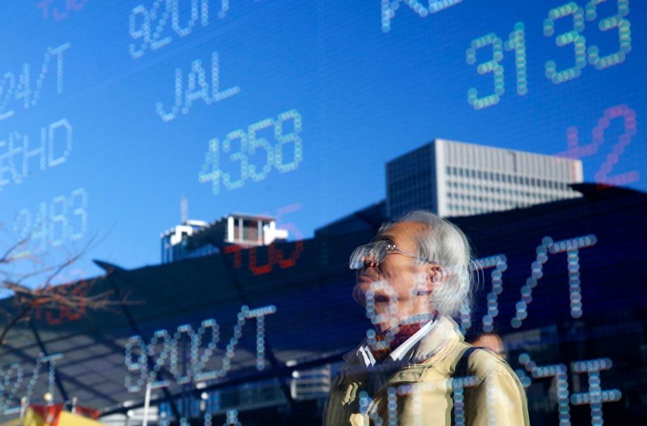 A man is reflected on an electronic stock indicator of a securities firm in Tokyo Tuesday Dec. 29 2015. Asian shares rose modestly on Tuesday shrugging off early losses though worries over China's slowdown and tumbling oil prices are overshadowing