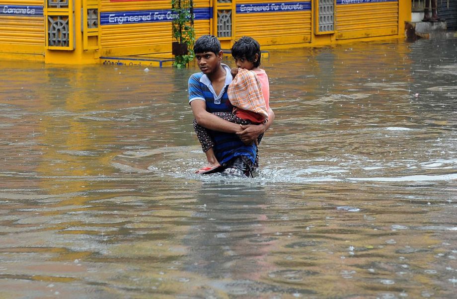 A boy carries a child and wades through a flooded street in Chennai in the southern Indian state of Tamil Nadu Wednesday Dec. 2 2015. Weeks of torrential rains have forced the airport in the state capital Chennai to close and have cut off several road