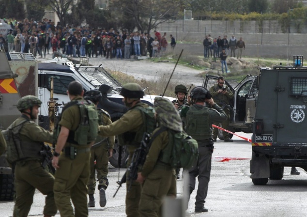 Palestinian youths look from afar as Israeli soldiers gather at the site of a previous stabbing attack near the flashpoint city of Hebron