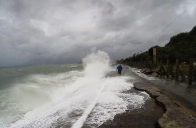 A resident walks past waves spilling over a wall onto a coastal road in the city of Legaspi in Albay province south of Manila on Monday as Typhoon Melor approaches the city