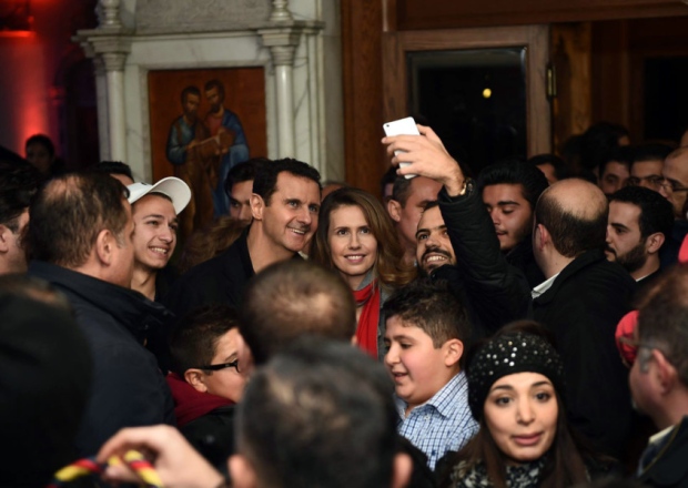 A photgraph from the official Facebook page of the Syrian presidency shows Bashar al Assad and his wife Asma al Assad pose for a selfie with a Syrian man as they attend a Christmas choral presentation at the Lady of Damascus Catholic Church in the Syrian