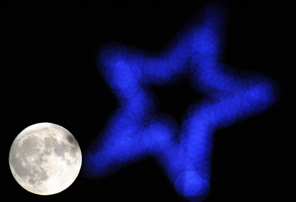 The moon is seen beyond an illuminated star on top of a Christmas tree in Hartley Wintney 40 miles west of London