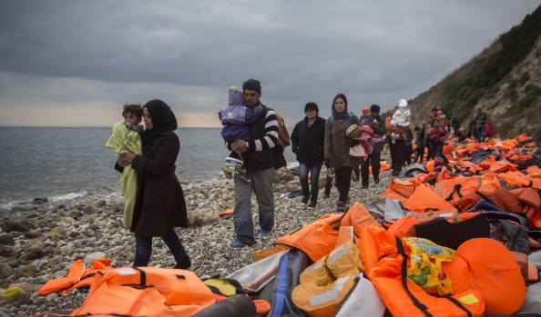 Refugees and migrants walk along a beach after crossing a part of the Aegean on a dinghy from Turkey to the Greek island of Lesbos