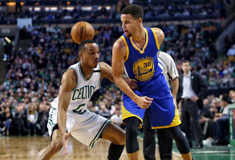 Steph Curry passes behind his back as Celtics guard Avery Bradley plays defence