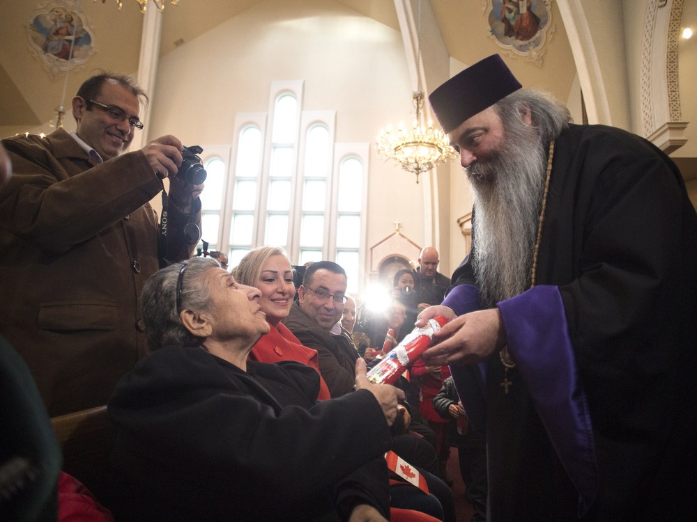 Armenian Orthodox Priest Meghrig Parikian right hands a Christmas chocolate to Gerget Prtoyan during a service at the St. Mary Armenian Apostolic Church where Syrian refugees arrived this morning in Toronto on Friday Dec. 11 2015