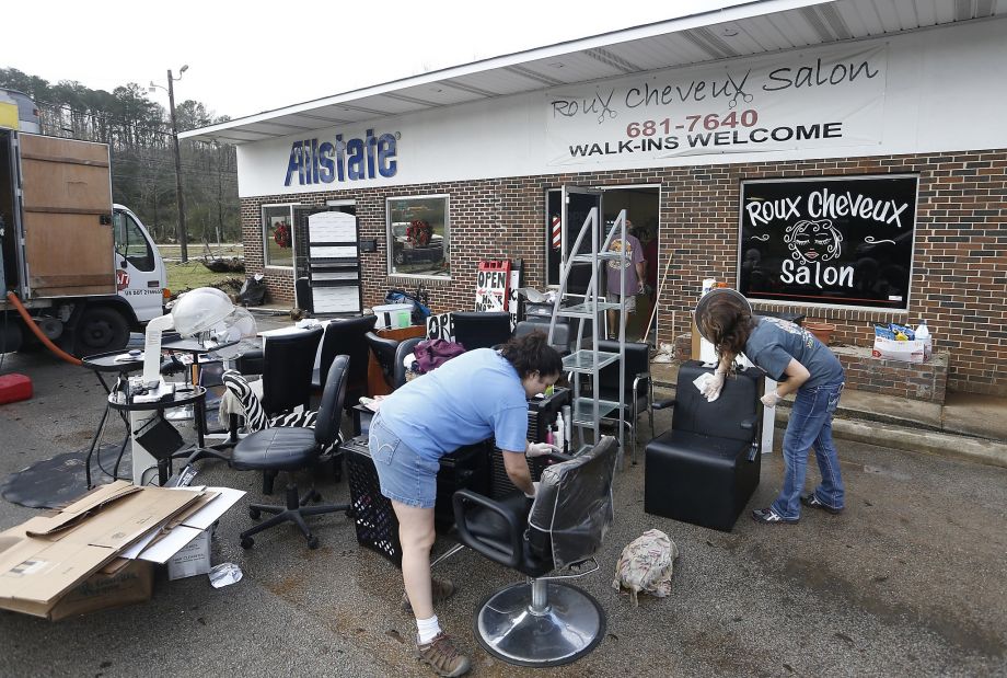 Lena Yawn and Becky Wester clean items from their friend Michele Smith’s business Roux Cheveux Salon in Pinson Ala. after floodwaters damaged commercial properties in the town