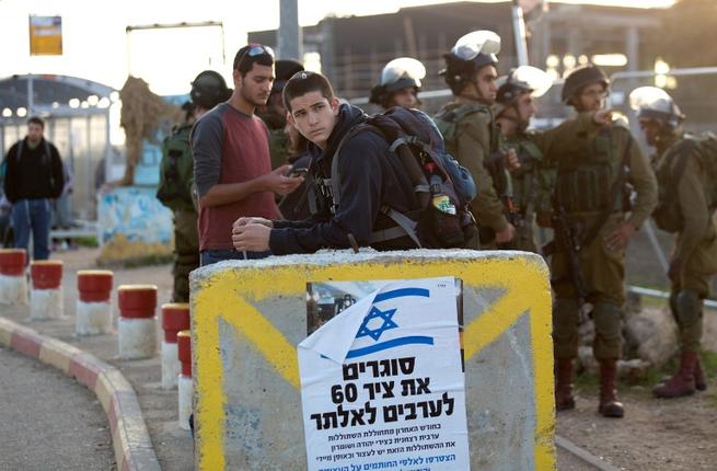 Israeli soldiers stand next to commuters at a bus station where a Palestinian attacker stabbed an Israeli woman before being shot dead by Israeli security forces near the Gush Etzion junction south of Jerusalem