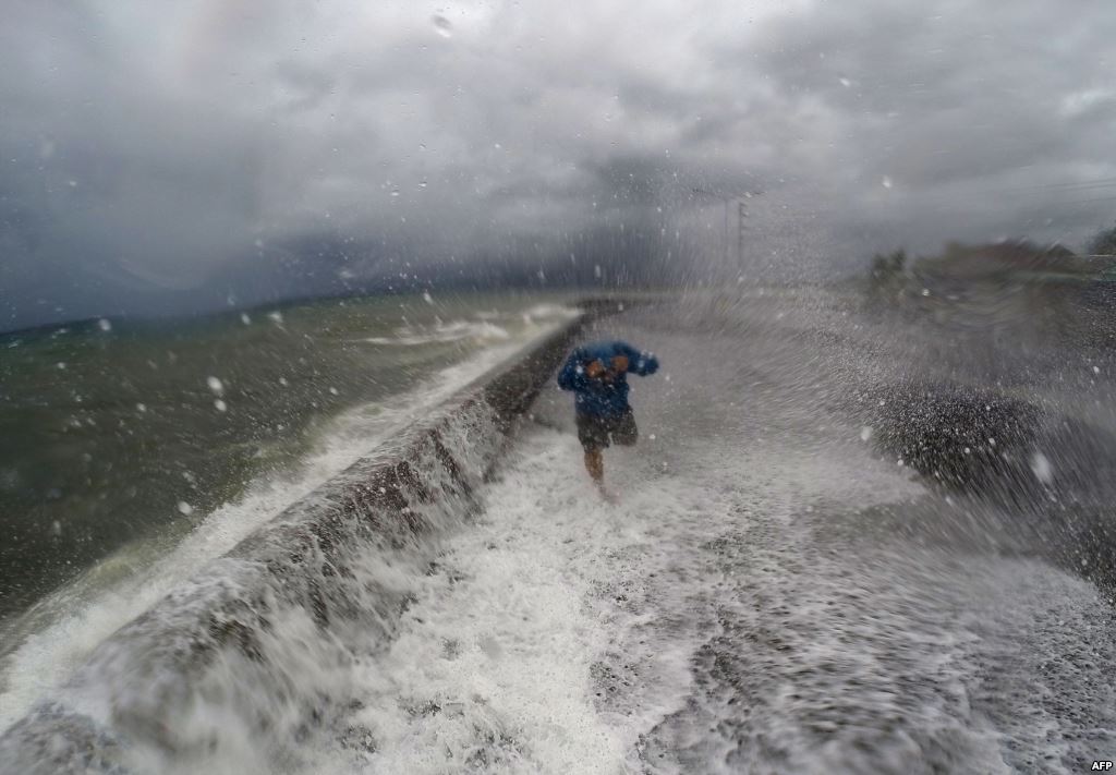 A resident walks past waves spilling over a wall onto a coastal road in the city of Legaspi in Albay province south of Manila