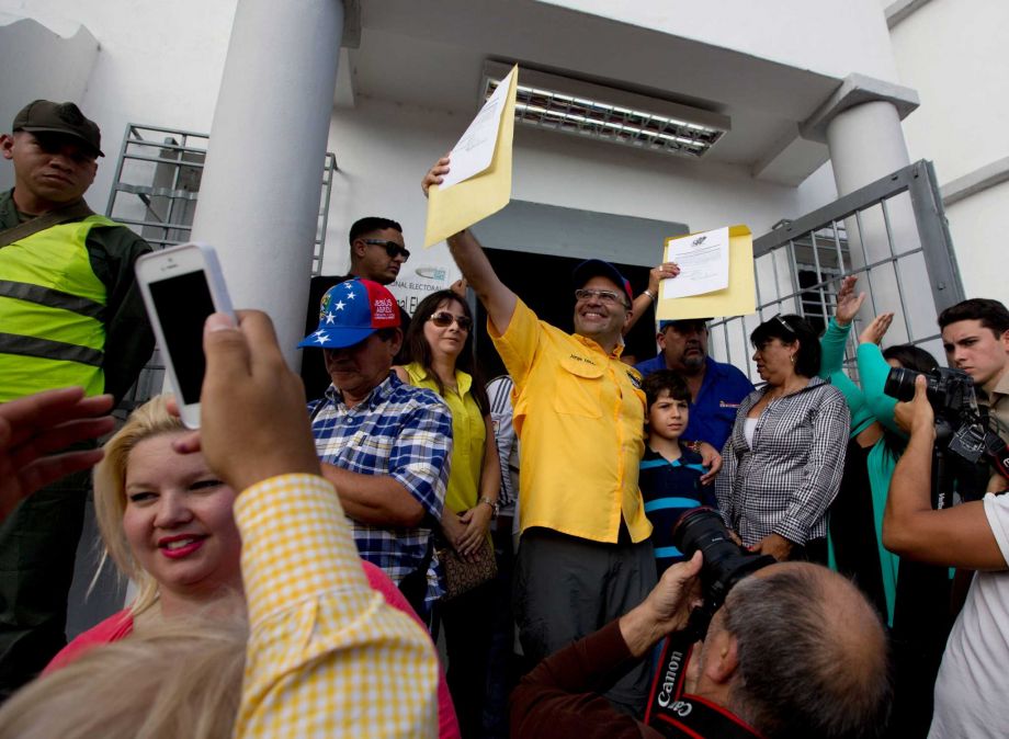 Newly elected opposition congressman Jorge Millan center holds up his credentials after receiving them from the National Electoral Council in Caracas Venezuela Wednesday Dec. 9 2015. The Democratic Unity opposition coalition secured by a sing