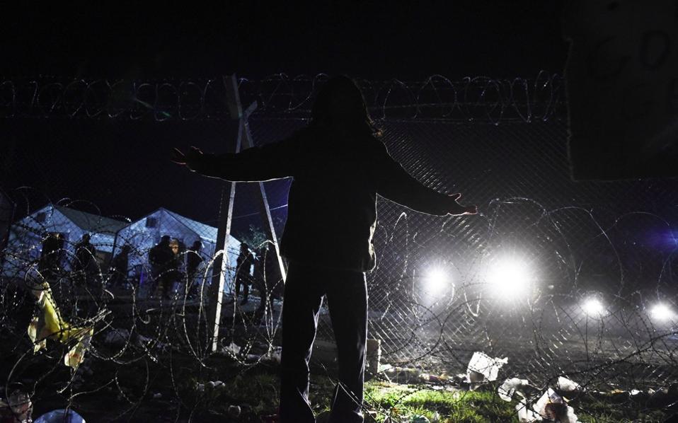 A man stands in front of the border fence as migrants from Morocco demand to cross the Greek-FYROM border near the northern Greek village of Idomeni Monday