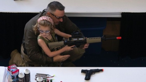 A man shows a girl how to hold an airsoft gun during the NRA Youth Day