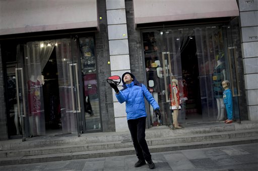 A salesperson plays with balls to attract visitors to his shop selling fashion clothes and souvenirs at Qianmen Street a popular tourist spot in Beijing Wednesday Jan. 20 2016. Asian stock prices tumbled Wednesday after the IMF's lower growth forecas