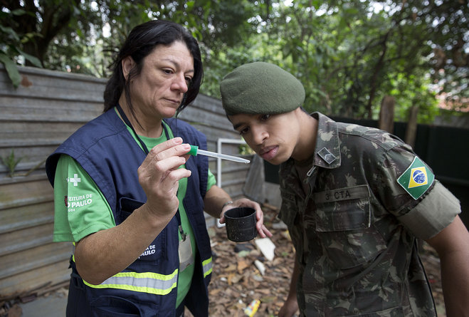 A health agent from Sao Paulo's Public health secretary shows an army soldier Aedes aegypti mosquito larvae that she found during clean up operation against the insect which is a vector for transmitting the Zika virus in Sao Paulo Brazil Wednesday Ja