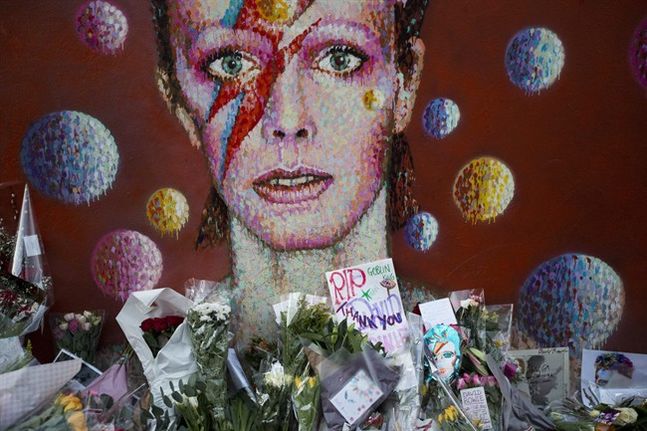 Tributes lie beneath a mural of British singer David Bowie by artist Jimmy C in Brixton south London Tuesday Jan. 12 2016. Bowie the other-worldly musician who broke pop and rock boundaries with his creative musicianship nonconformity striking visu