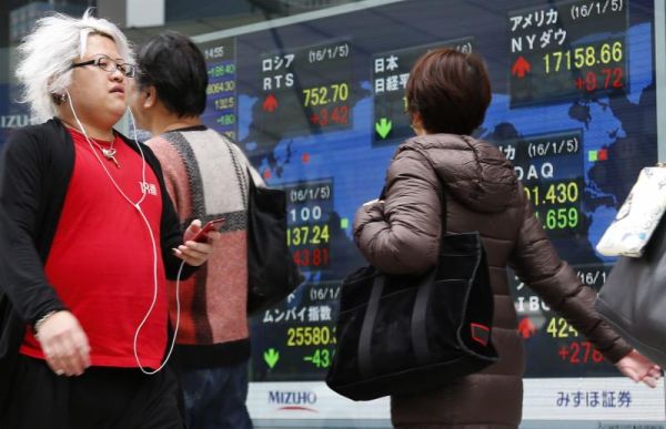 People walk past an electronic stock indicator