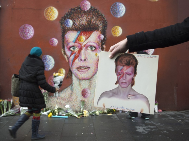 A man holds David Bowie's album Aladdin Sane in front of a mural of Bowie on the wall of a Morley's store in Brixton London the singers birthplace after the rock star died following an 18-month battle with cancer. PRESS ASSOCIATION