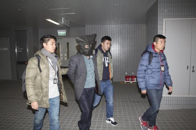 Forty-four-year-old Deyun Shi is escorted by plainclothed police officers in Hong Kong