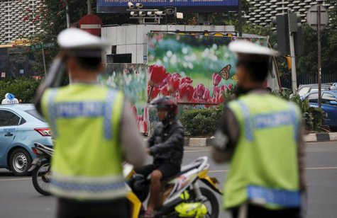 Indonesian police stand near a boarded up police box that was hit during yesterday's gun and bomb attack in central Jakarta