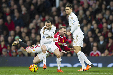 Manchester United's Wayne Rooney centre is brought down by Swansea City's Leon Britton left as Federico Fernandez looks on during the English Premier League soccer match between Manchester United and Swansea City at Old Trafford Stadium Manchester E