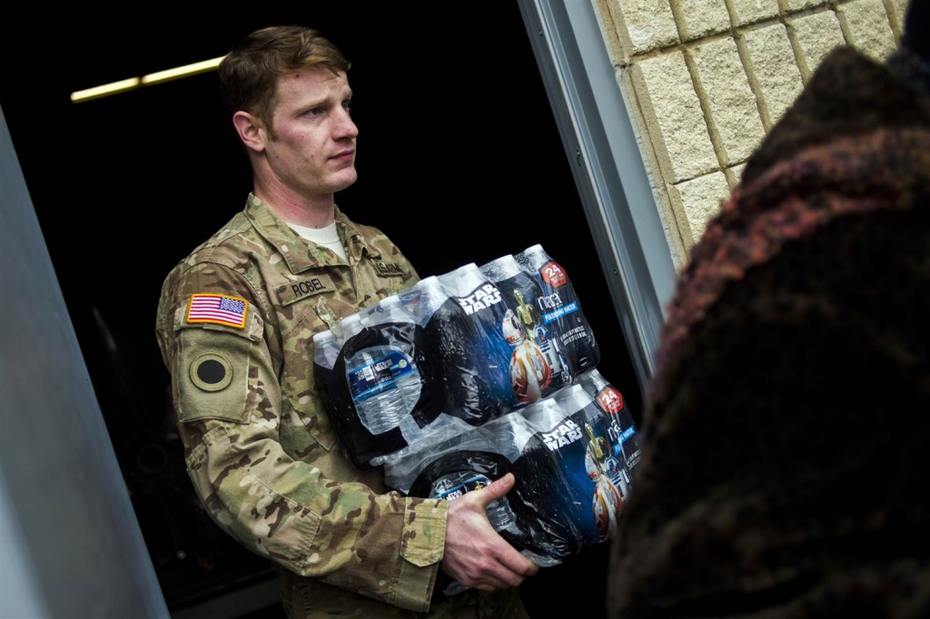 Michigan National Guard Staff Sgt. Stephen Robel helps carry a case of water to the vehicle of Flint resident Karand Houston Jake May