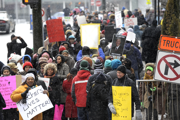 Burton International Academy computer advanced teacher Denice McGee bottom left holds a sign as she and other protesters wait to cross the street Wednesday