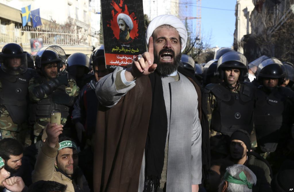 Surrounded by policemen a Muslim cleric addresses a crowd during a demonstration to protest the execution of Saudi Shi'ite Sheikh Nimr al-Nimr shown in the poster in front of the Saudi embassy in Tehran Iran Jan. 3 2016