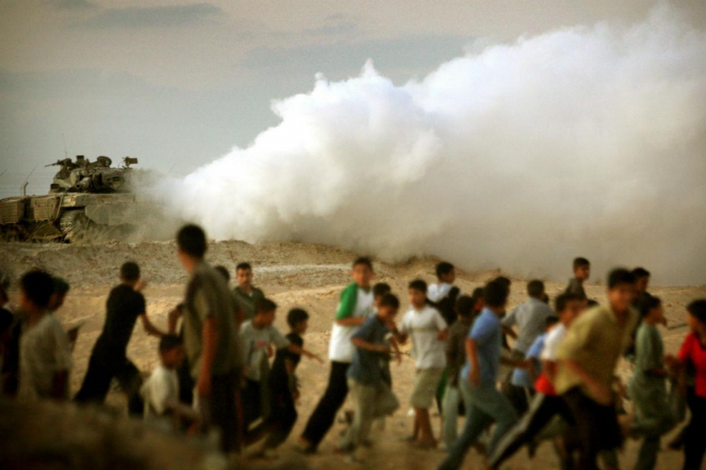 Palestinians run from an Israeli army tank guarding the Jewish settlement of Neve Dekalim southern Gaza Strip