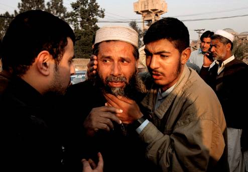 People comfort a man who lost a family member in a suicide attack in Mardan Pakistan