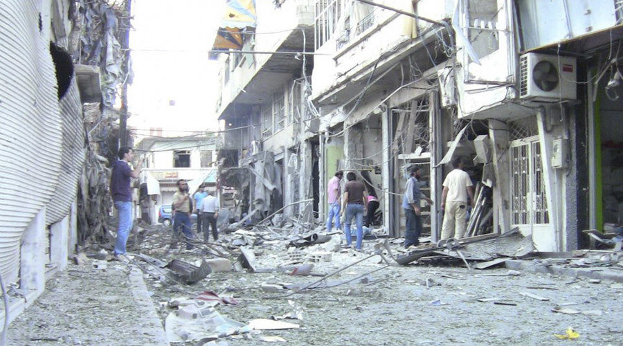 People look at damaged buildings at Al Zabadani