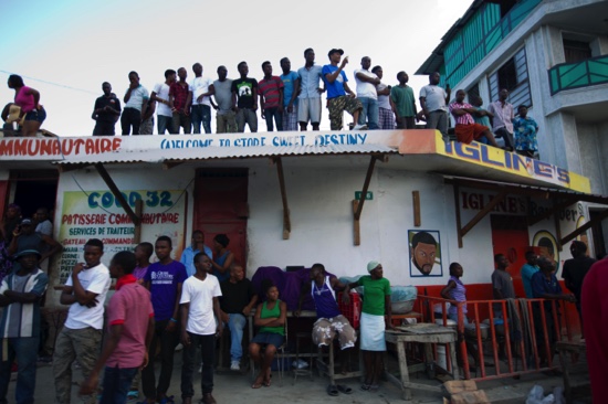 Residents watch a crowd protesting against President Michel Martelly’s government in Port-au-Prince Haiti