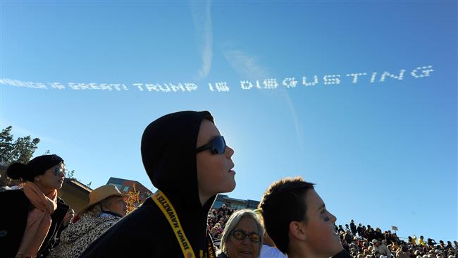 Rose Parade spectators watch as airplane skywriters write a message across the sky that reads “America is great! Trump is disgusting.”