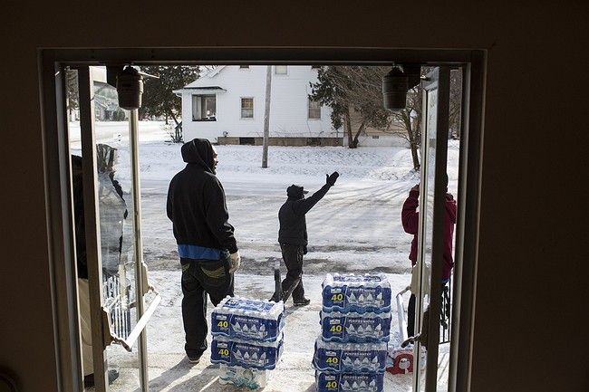 Aaron Dunigan waves to cars as volunteers hand out water at the Joy Tabernacle Church on Monday Jan. 11 2016 in Flint Mich. Michigan Gov. Rick Snyder pledged Monday that officials would make contact with every household in Flint to check whether resid