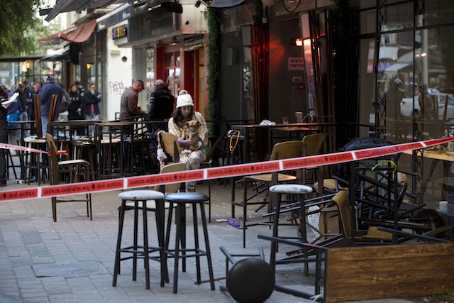 An Israeli eye witness sits with her dog at the scene of a shooting attack in Tel Aviv Israel Friday Jan. 1 2016. A gunman opened fire at a popular bar in the central Israeli city of Tel Aviv on Friday afternoon killing two and wounding at least thre