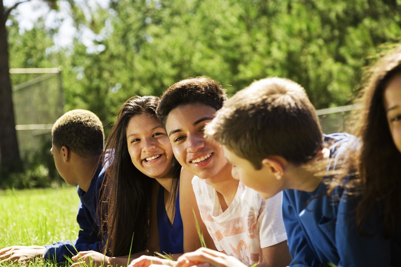 Group of racially diverse boys and girls lying on grass and conversing