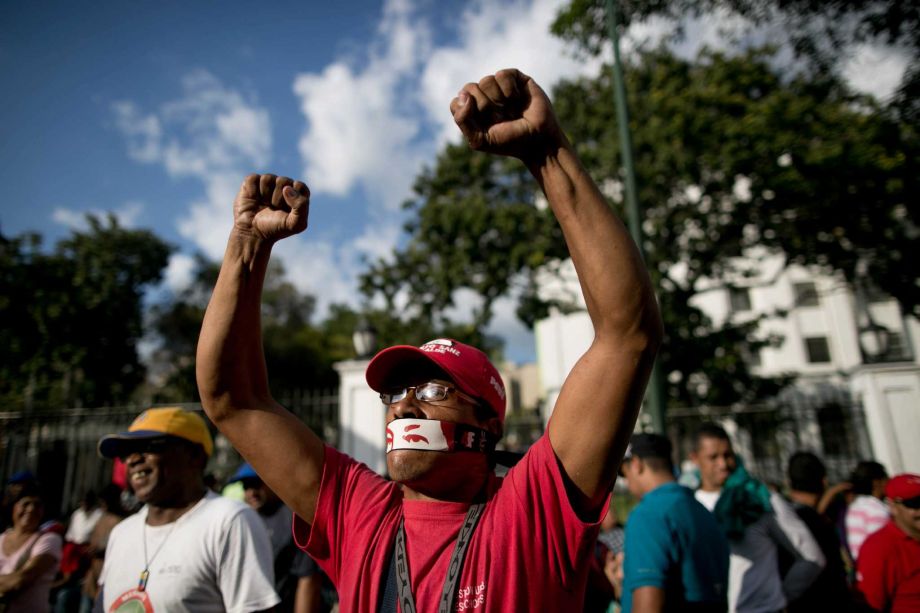 A government supporter wears a piece of tape over his mouth decorated with an image of the eyes of Venezuela's late President Hugo Chavez outside Miraflores presidential palace in Caracas Venezuela Tuesday Jan. 5 2016 to protest the swearing-in