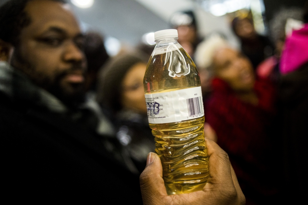 Pastor David Bullock holds up a bottle of Flint water as Michigan State Police hold a barrier to keep protestors out of the Romney Building where Gov. Rick Snyder's office resides on Thursday Jan. 14 2016 in Lansing Mich. More than 150 people tried