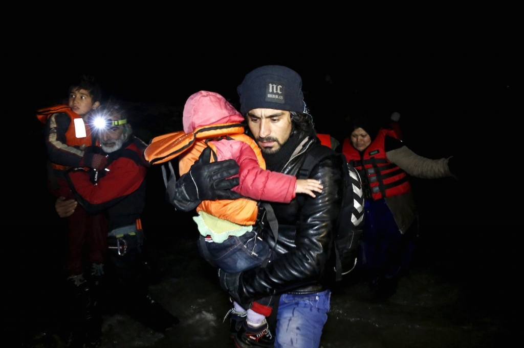 An Afghan migrant carries a child as he arrives with other Afghan migrants on a raft on the Greek island of Chios early today. – Reuters pic