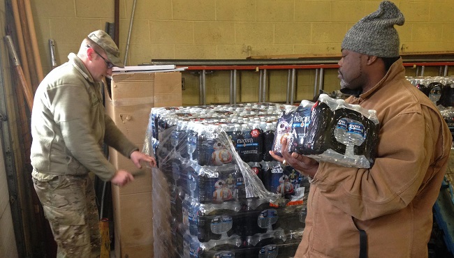 Caption Staff Sgt. William Phillips with the Michigan National Guard left assists a resident at a water distribution center Wednesday Jan. 13 2016 at a fire station in Flint Michigan. Gov. Rick Snyder activated the Natonal Guard last week to help