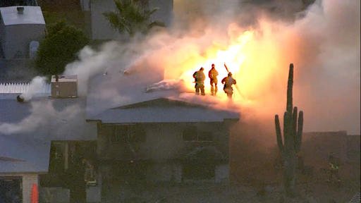 This image made from video provided by KNXV ABC-15 Arizona shows firefighters atop a house engulfed in flames in Phoenix on Tuesday Feb. 23 2016. Police and firefighters braved bullets and flames as they responded to the fatal shooting and house fire