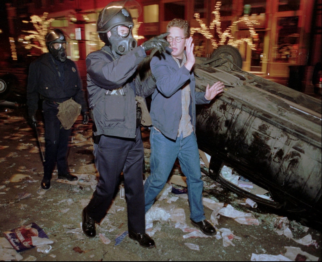 Denver Police Department officers wearing riot gear lead an unidentified man away from an overturned car during a riot in Denver's tony Larimer Square after the Denver Broncos defeated the Green Bay Packers to win Super Bowl XXXII in this file