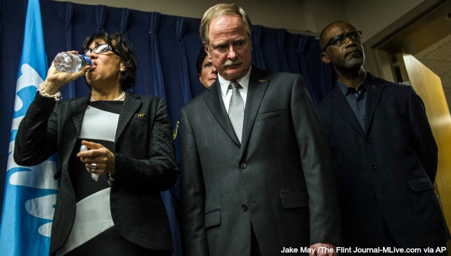 Flint Mayor Karen Weaver drinks from a bottle of water beside Michigan Department of Environmental Quality Director Keith Creagh as Gov. Rick Snyder fields questions from reporters about the Flint water crisis during a