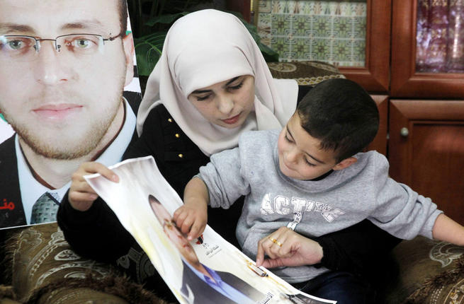 Fayha Shalash the wife of Palestinian journalist Muhammed al-Qiq sits with her son at her home in the West Bank village of Dura