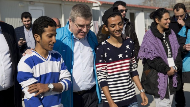 IOC President Thomas Bach chats with two young refugees during his visit at a refugee camp in Athens