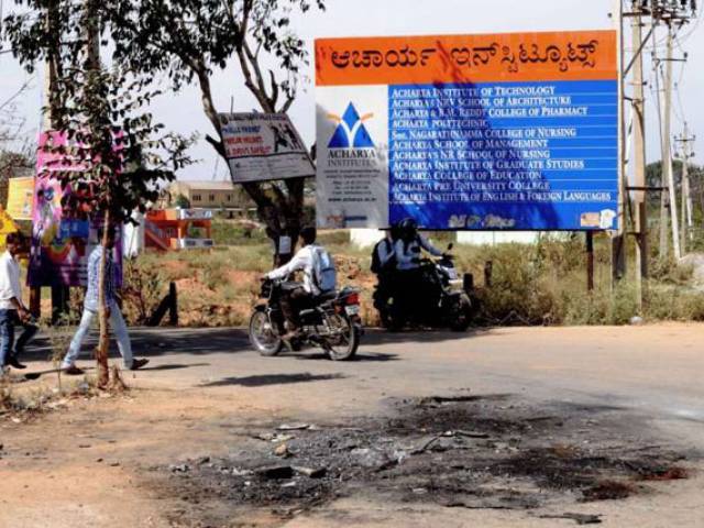 Indian pedestrians walk past the spot where a vehicle was set ablaze by a mob in Bangalore on Feb 2