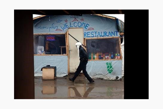 A migrant walks past a makeshift restaurant in a camp set outside Calais France Monday Feb. 22 2016. Authorities issued an expulsion order Friday for hundreds of migrants living in this huge swath of the Calais camp demanding that they remove their