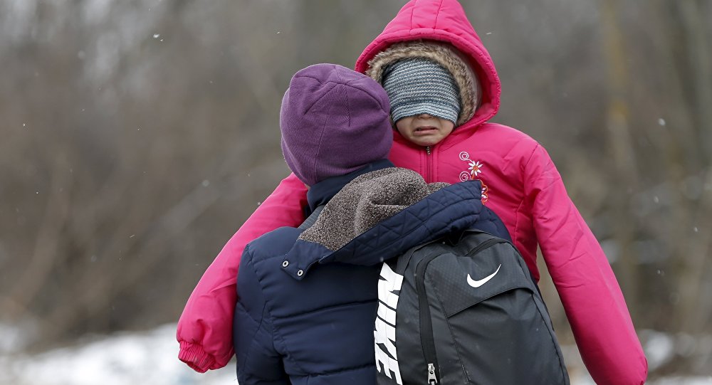 A migrant carries a child as they walk through a frozen field after crossing the border from Macedonia near the village of Miratovac Serbia