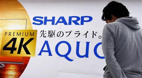 A shopper walks in front of an advertisement of Sharp's Aquos at an electronics store in Tokyo Thursday Feb. 25 2016. Troubled Japanese electronics maker Sharp has agreed to a takeover offer from Taiwanese company Hon Hai also known as Foxconn Japane