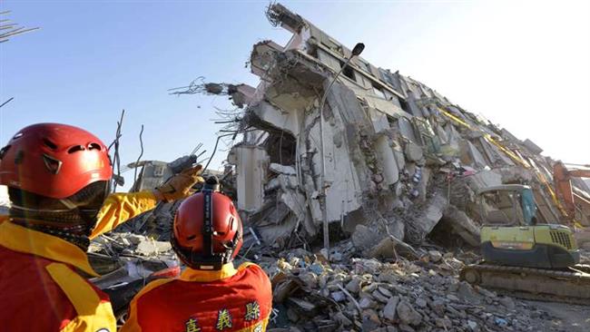 Two rescue workers stand next to the remains of a building complex that collapsed in the 6.4-magnitude earthquake in the southern Taiwanese city of Tainan